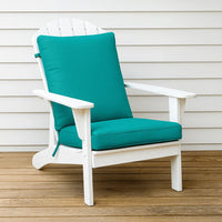 White chair with teal cushions on a wooden deck against a beige wall.
