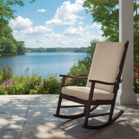 An outdoor rocking chair with cream cushions and a dark brown wooden frame sits on a tiled porch overlooking a scenic lake with trees and a blue sky.