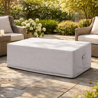 Light gray custom rectangular fire pit cover on a stone patio, surrounded by wicker patio furniture and garden landscaping
