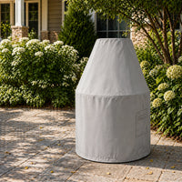 Custom Traditional Round Chiminea Cover in light gray, shown on a stone patio surrounded by lush garden greenery