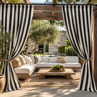 Black and white vertically striped patio curtains hanging on a wooden pergola frame over a modern outdoor sectional sofa in a garden setting.