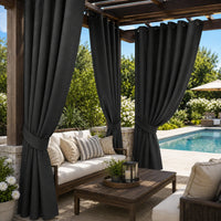 Dark charcoal gray patio curtains hanging on a wooden pergola over a furnished outdoor seating area with a pool in the background.