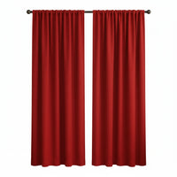 A pair of bright red curtain panels hanging on a black rod over a window in a styled living room with a beige armchair, side table, and plant.