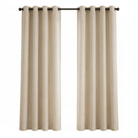A pair of beige grommet-top window curtains hanging on a black rod in a bright room with a window, potted plant, and small side table.