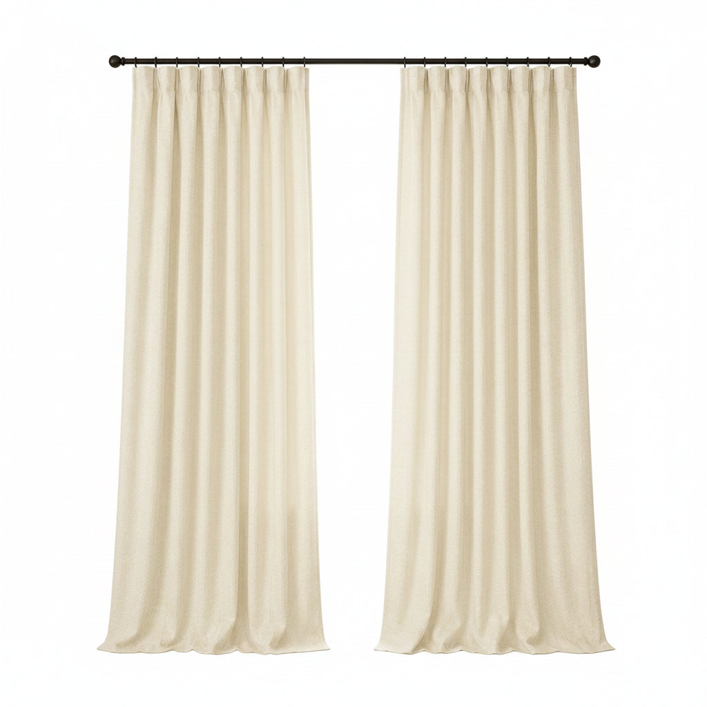 A pair of cream-colored curtain panels hanging from a black rod in a bright, modern room with a window, side table, and armchair.