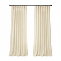 A pair of cream-colored curtain panels hanging from a black rod in a bright, modern room with a window, side table, and armchair.