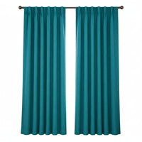 A pair of teal window curtain panels hanging on a dark rod in a bright room with a window, side table, framed art, and part of a sofa visible.